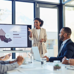 Business meeting, businesswoman and presentation on screen of tv in modern boardroom with colleagues. Workshop, speech and black woman or speaker speaking with coworkers in conference room.