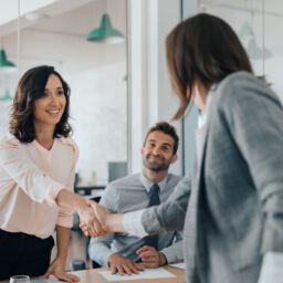 Smiling young businesswoman shaking hands with a coworker during a meeting with colleagues around a table in an office boardroom