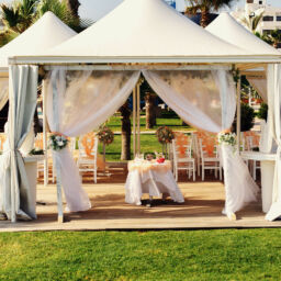 Luxurious wedding tent with haze peachy fabric and floral decorations near the palm trees and blue ocean